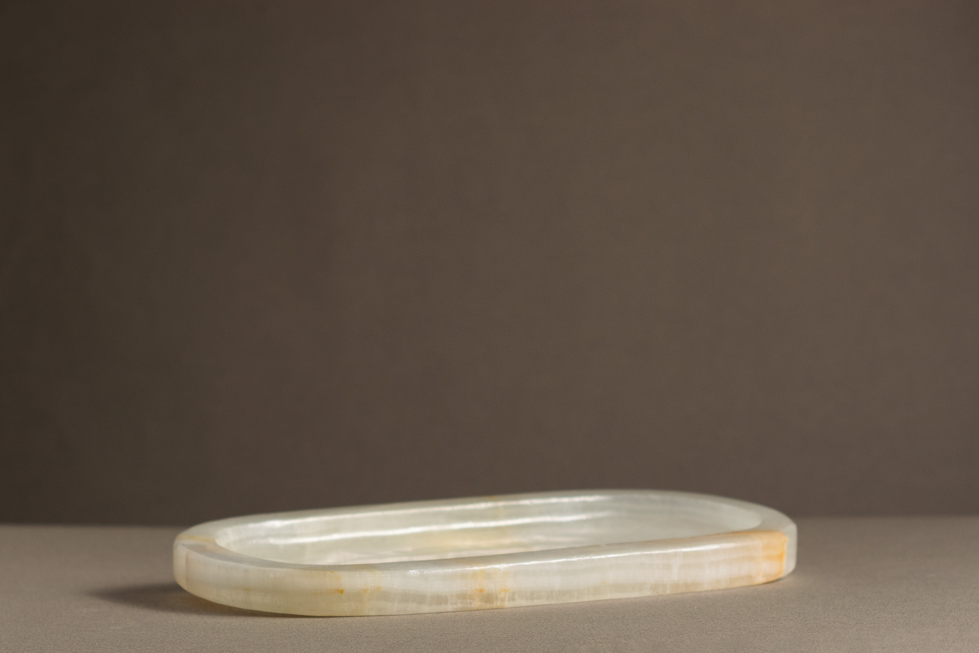 Side view of the Aura White Onyx Tray highlighting its oval shape and polished finish.