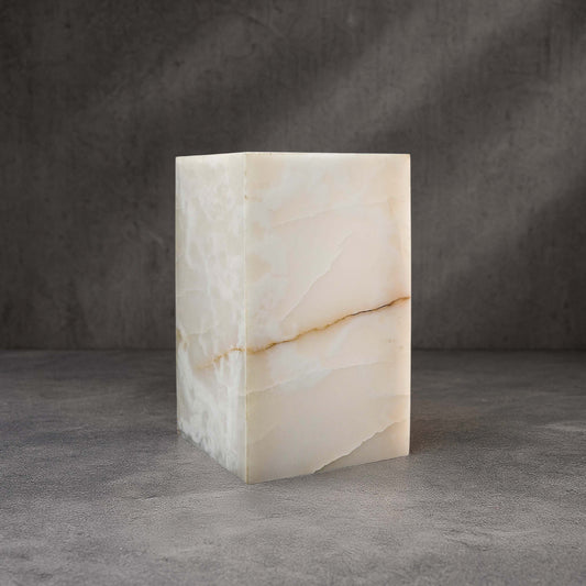 White Onyx column side table styled in a contemporary living space, showcasing luminous natural stone and warm golden veining.