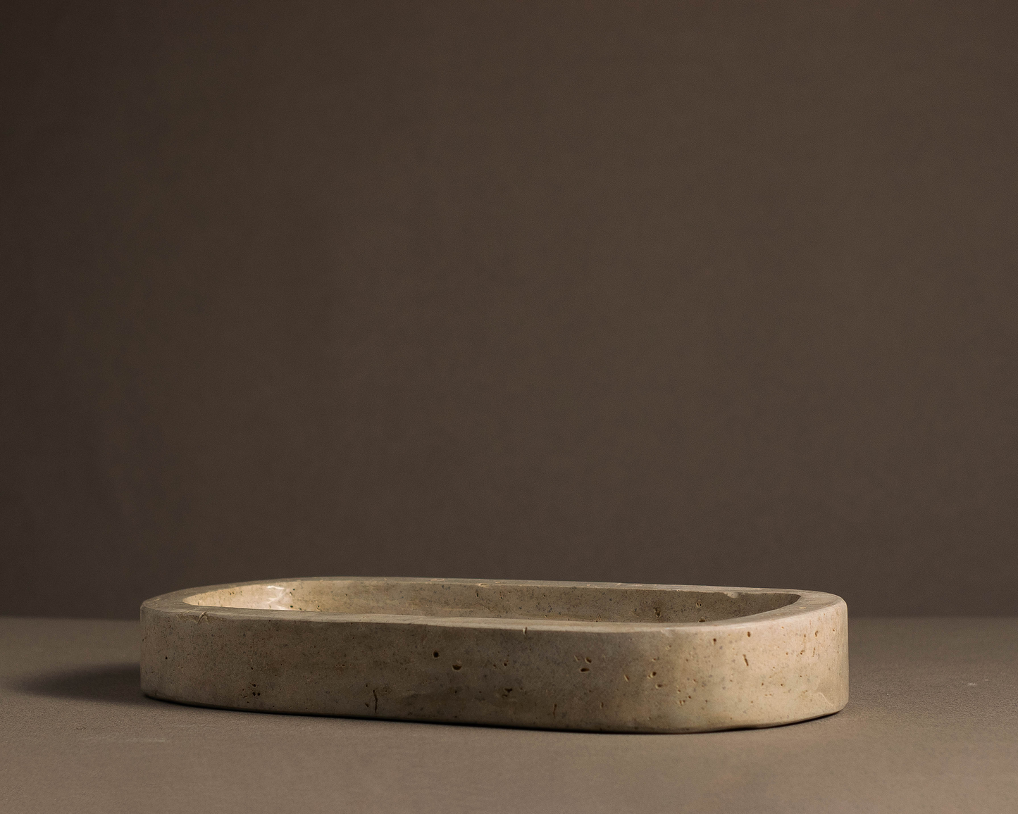 Side view of the Oval Travertine Tray showcasing its slim handcrafted stone profile.