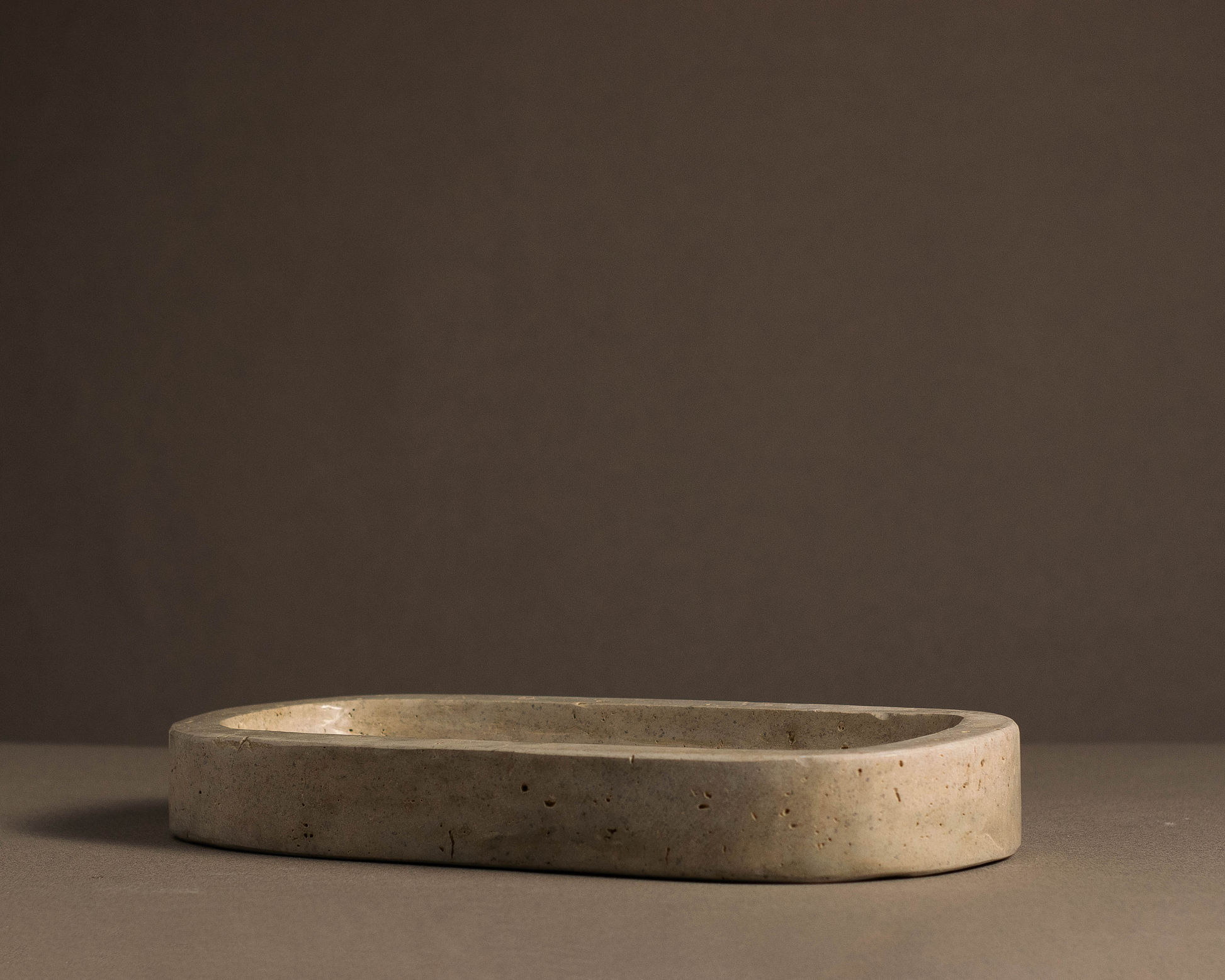 Side view of the Oval Travertine Tray showcasing its slim handcrafted stone profile.